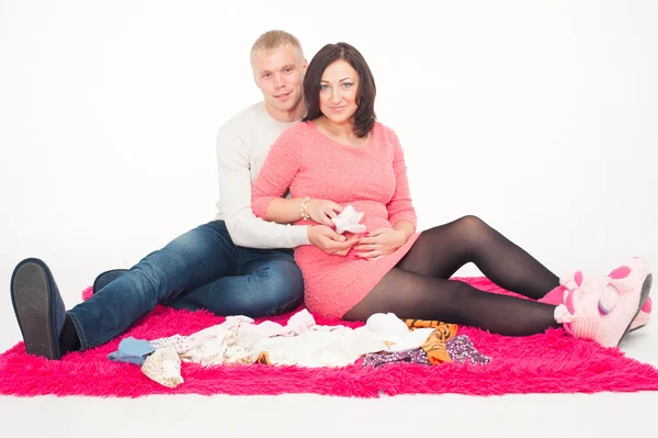 Szczęśliwa kobieta w ciąży z mężem, patrząc na ubrania dla ich przyszłego dziecka — Zdjęcie stockowe