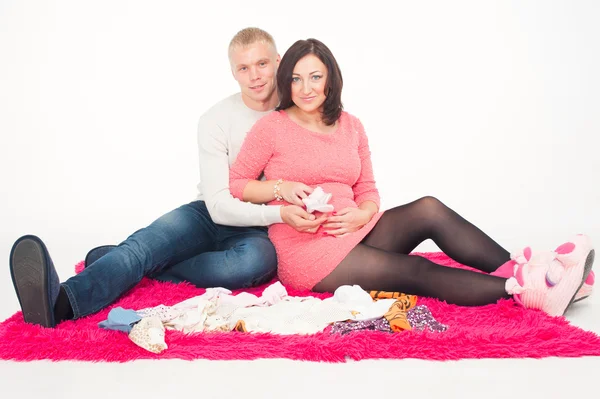 Happy pregnant woman with her husband looking at clothes for their future child — Stock Photo, Image