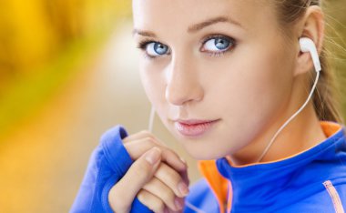 Sporty woman runner listens to music in nature clipart