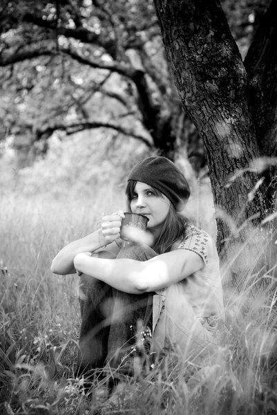 Black and white portrait of beautiful young woman is enjoying her cup of coffee in green park