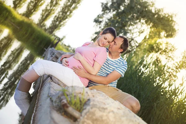 Casal grávida relaxante por lago — Fotografia de Stock