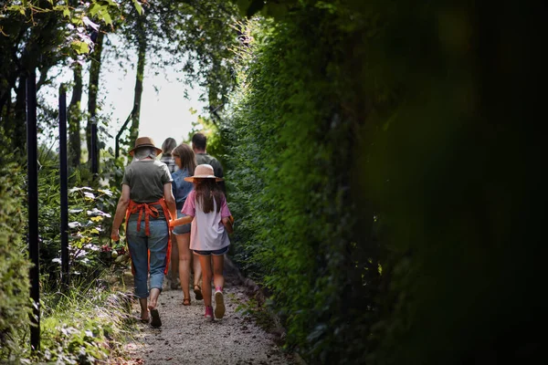 Vista trasera de jóvenes y viejos agricultores o jardineros felices llevando su cosecha al aire libre en la granja comunitaria. —  Fotos de Stock