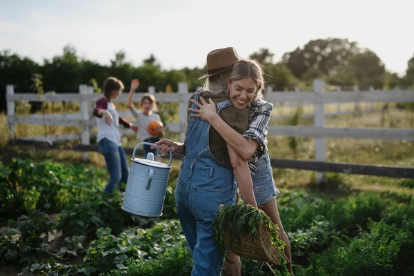 Счастливая средняя взрослая женщина-фермер обнимает свою старшую подругу, держа корзину с овощами на улице на ферме.. — стоковое фото