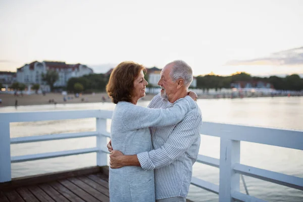 Cuplu senior fericit în dragoste îmbrățișarea în aer liber pe dig pe mare, uitându-se unul la celălalt . — Fotografie, imagine de stoc