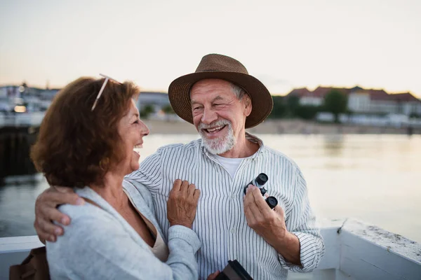 Un cuplu senior fericit îmbrățișându-se în aer liber pe dig pe mare, uitându-se unul la celălalt și râzând . — Fotografie, imagine de stoc