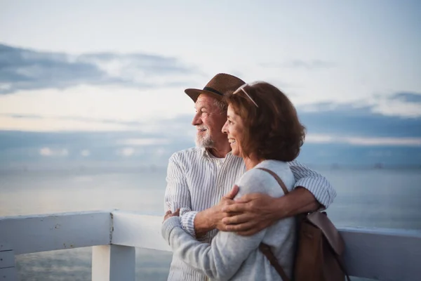 Porträtt av glada äldre par i kärlek kramar utomhus på piren vid havet, tittar på utsikten, sommarsemester. — Stockfoto