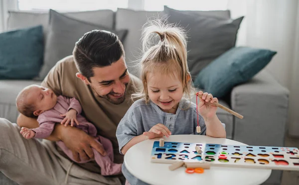 Felice giovane uomo prendersi cura del suo bambino appena nato e la piccola figlia in casa, congedo di paternità. — Foto Stock