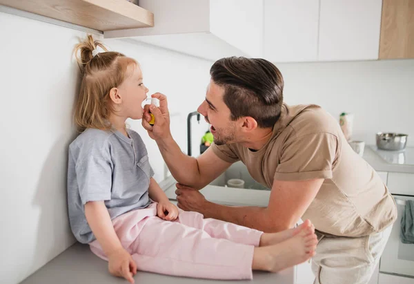 Jonge vader die thuis voor zijn dochtertje zorgt, medicijnen gebruikt. — Stockfoto