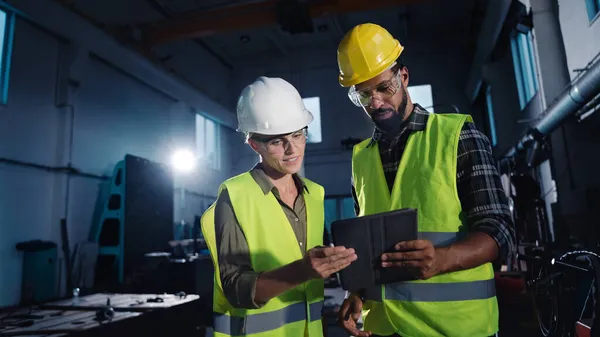 Vue en angle bas des inspecteurs industriels avec tablette effectuant un contrôle général et parlant à l'intérieur à l'atelier de métal. — Photo