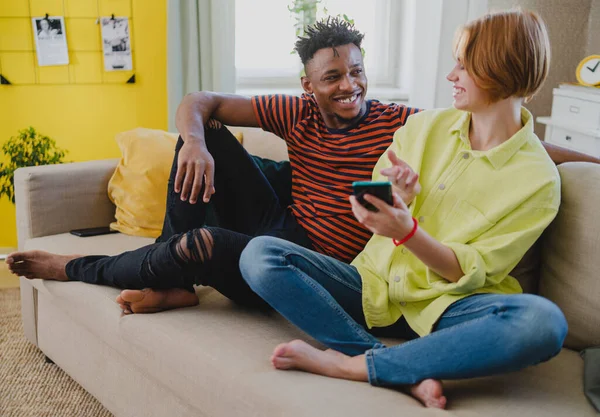 スマートフォンを使った若い夫婦が自宅で楽しみ、ソーシャルネットワークを一緒にチェックする. — ストック写真