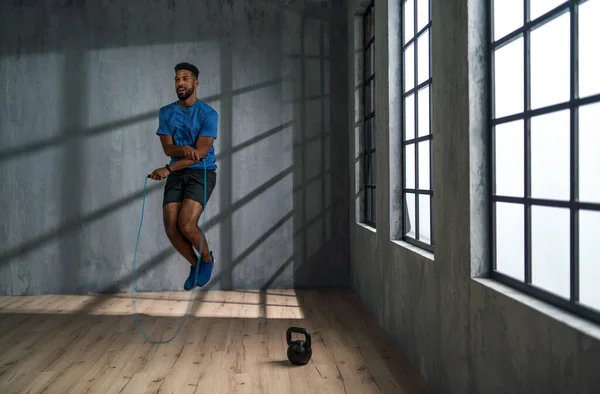 Pemuda Afrika Amerika olahragawan menggunakan melompat tali di dalam ruangan, latihan konsep pelatihan. — Stok Foto