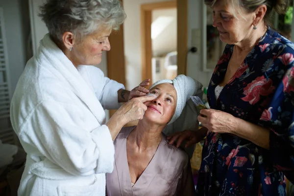 Happy senior women friends in bathrobes applying anti wrinkle patches indoors at home, selfcare concept. — Stock Photo, Image