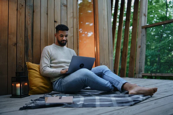 Šťastný mladý muž s laptopem odpočívá venku v domku na stromě, víkend pryč a koncept vzdálené kanceláře. — Stock fotografie