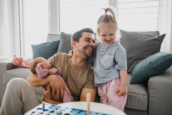 Счастливый молодой человек заботится о своем новорожденном ребенке и маленькой дочери в помещении дома, отпуск по уходу за ребенком. — стоковое фото