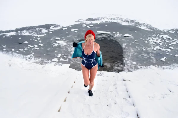 Hochwinkelaufnahme einer aktiven Seniorin im nassen Badeanzug, die im Winter im Freien Treppen hochläuft, Kältetherapie-Konzept. — Stockfoto