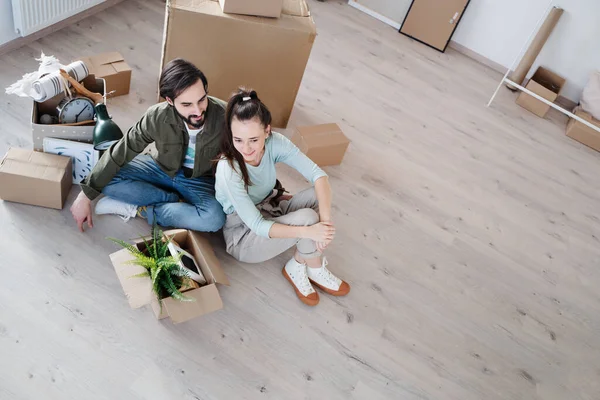 Hoge hoek uitzicht van jong paar met dozen zitten op de vloer bij het verhuizen in nieuwe flat, nieuw huis en verhuizing concept. — Stockfoto