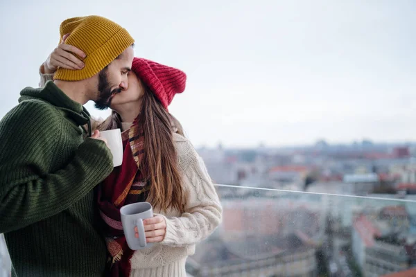 Jovem casal com café de pé e beijando ao ar livre na varanda com vista urbana — Fotografia de Stock