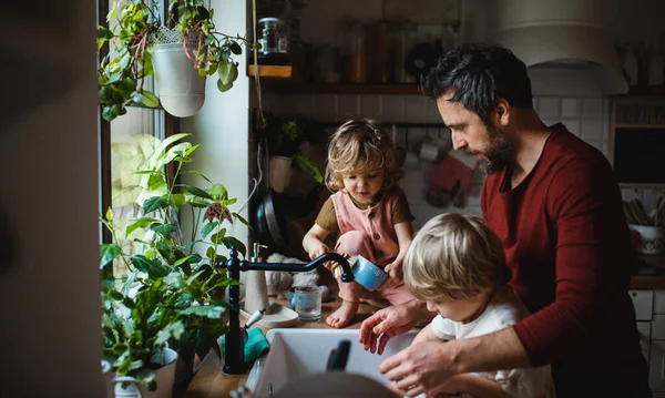 Padre maduro con dos niños pequeños lavando platos en el interior de casa, concepto de tareas diarias. — Foto de Stock