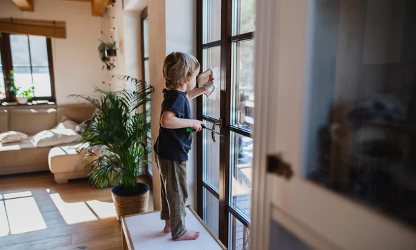 Side view of little boy cleaning windows indoors at home, daily chores concept. — Stock Photo, Image