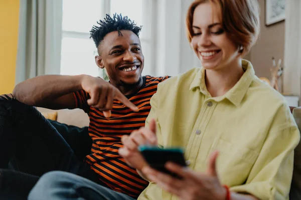 スマートフォンを使った若い夫婦が自宅で楽しみ、ソーシャルネットワークを一緒にチェックする. — ストック写真