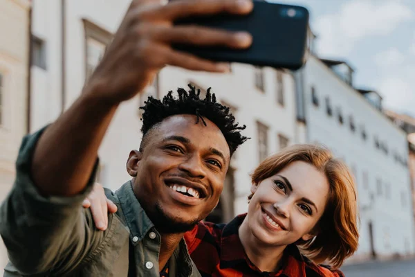 Jovem casal biracial fazendo selfie para redes soiais ao ar livre na cidade. — Fotografia de Stock