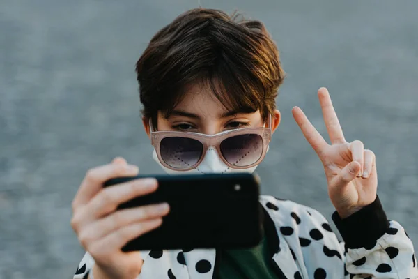 Preteen ragazza in occhiali da sole prendendo selfie per i social network al di fuori in città, concetto coronavirus. — Foto Stock