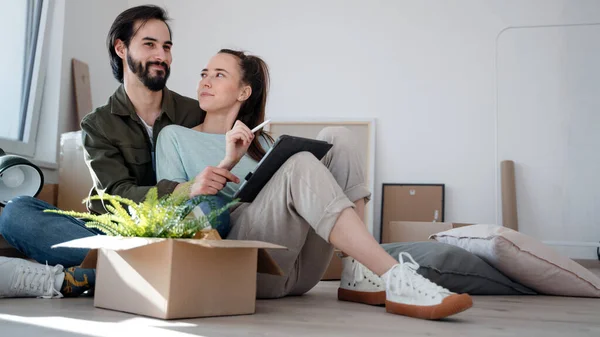 Jeune couple avec tablette assis sur le sol et la planification lors du déménagement dans un nouvel appartement. — Photo