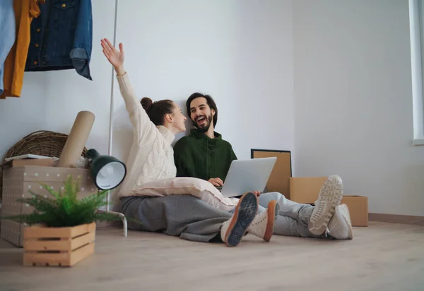 Jeune couple avec ordinateur portable assis sur le sol et la planification lors du déménagement dans un nouvel appartement. — Photo