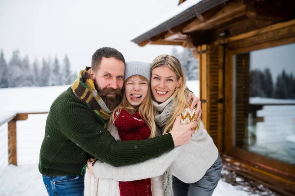 Porträtt av lycklig familj med liten dotter utomhus i vinterstuga, tittar på kamera. — Stockfoto