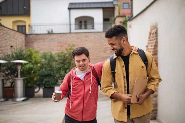 Joven con síndrome de Down y su amigo mentor caminando y hablando al aire libre —  Fotos de Stock