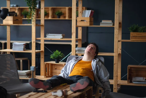 Young tired man with Down syndrome sitting indoors at school, taking break — Stock Photo, Image
