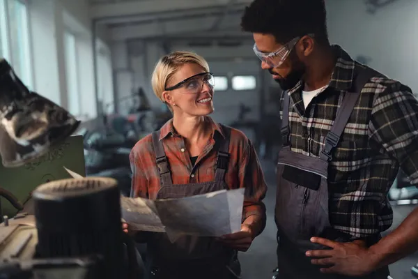 Porträt von jungen zweirassigen Industriekollegen, die in einer Metallwerkstatt arbeiten und dabei lächeln. — Stockfoto