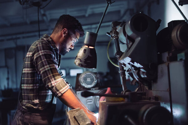 Portrait of young concentrated african american man working on cutter indoors in metal workshop.