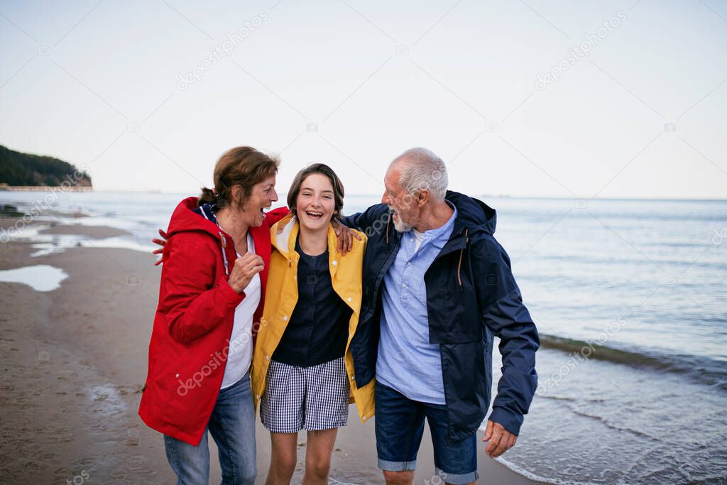 Senior couple and their preteen granddaughter hugging when walking on sandy beach.