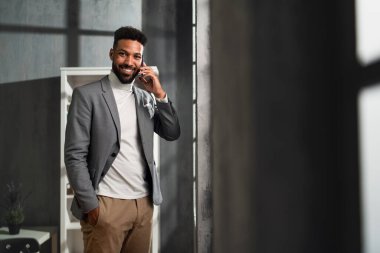 Ofisinde martphone ile kameraya bakan mutlu Afro-Amerikan iş adamı..
