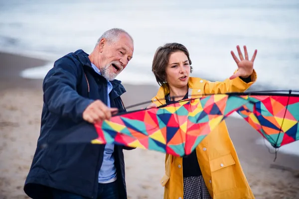 Senior man en zijn tiener kleindochter bereiden vlieger voor vliegen op zandstrand. — Stockfoto