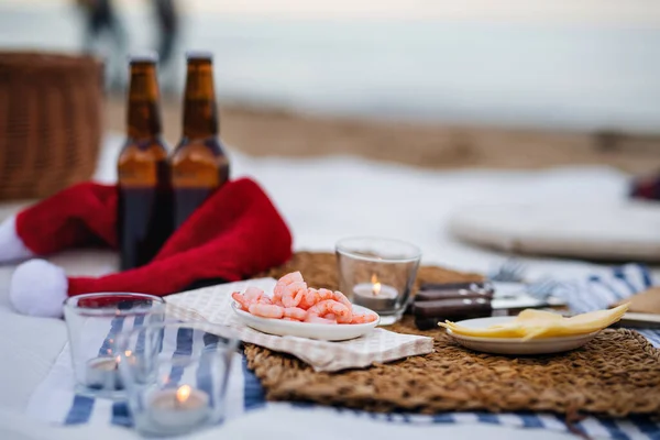 Beach picnic with schripms, beer, candles and santa hat. Exotic new year and Christmas — Stock Photo, Image