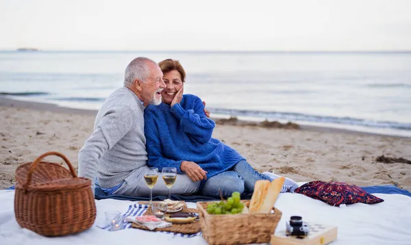 Szczęśliwa para seniorów w miłości siedzi na kocu i ma piknik na plaży nad morzem. — Zdjęcie stockowe