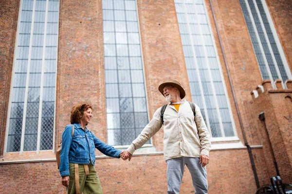 Низкий угол обзора счастливой пожилой пары влюбленных, держащихся за руки на улице в городе — стоковое фото