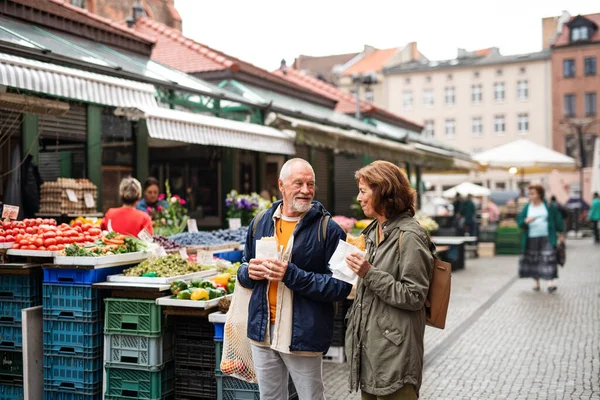 屋外市場で町で軽食と幸せなシニアカップル観光客の肖像画. — ストック写真