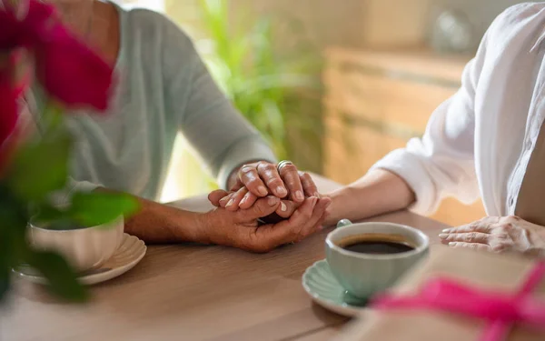 Κοντινό πλάνο της ηλικιωμένης μητέρας κρατώντας το χέρι της ενήλικης κόρης όταν έχουν καφέ μαζί σε εσωτερικούς χώρους στο σπίτι — Φωτογραφία Αρχείου