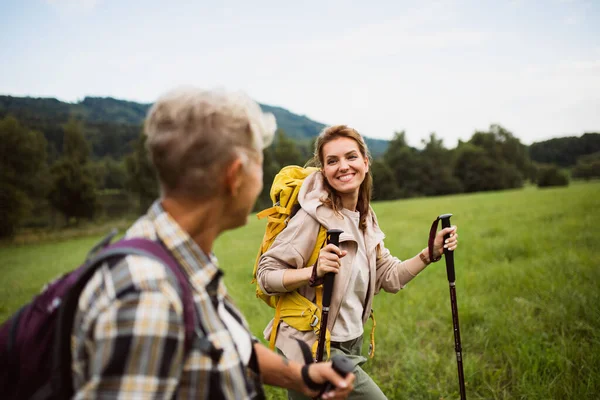 Glad medelvuxen kvinna med vandringsstavar vandring med aktiv senior mor utomhus i naturen. — Stockfoto