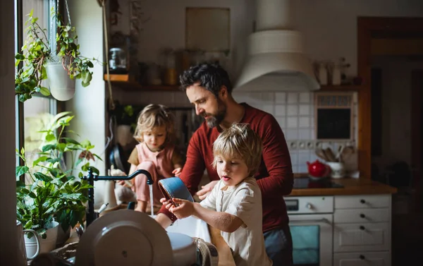 Padre maduro con dos niños pequeños lavando platos en el interior de casa, concepto de tareas diarias. — Foto de Stock