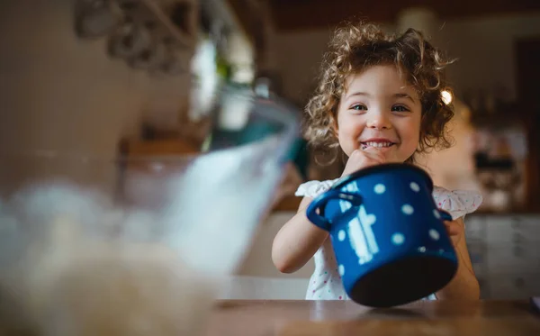 Gelukkig klein meisje zitten aan tafel binnen thuis, eten spaghetti en kijken naar de camera. — Stockfoto