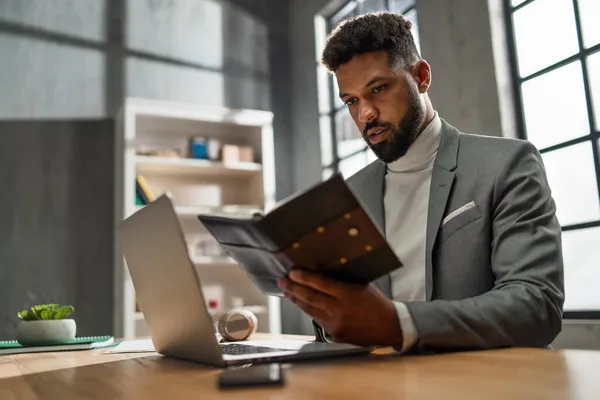Giovane uomo d'affari afroamericano con diario che lavora su laptop al chiuso in ufficio — Foto Stock