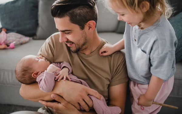 Mutlu genç adam evde yeni doğmuş bebeğine ve küçük kızına bakıyor. Babalık izni.. — Stok fotoğraf