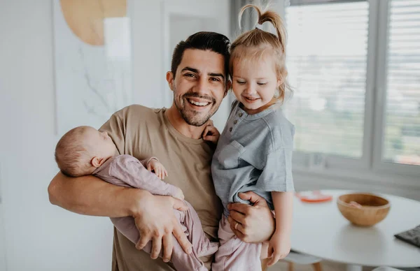 Mutlu genç adam evde yeni doğmuş bebeğine ve küçük kızına bakıyor. Babalık izni. — Stok fotoğraf