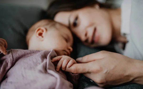 Jovem mãe feliz tocando sua menina recém-nascida, deitada no sofá dentro de casa. — Fotografia de Stock