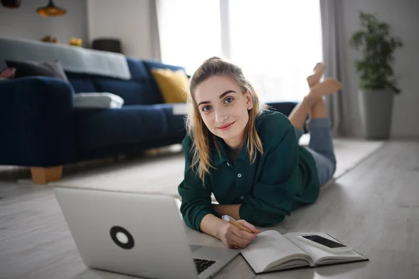 Молодая женщина студентка с ноутбуком и смартфоном на дому, домашний офис и обучение, глядя на камеру, — стоковое фото
