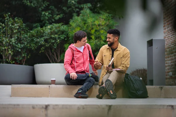 Glad ung man med Down syndrom och mentorskap vän sitter och pratar utomhus — Stockfoto
